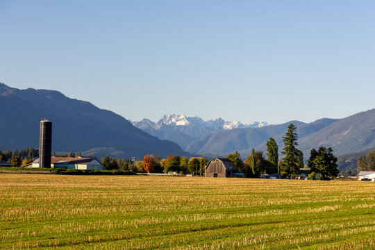 Farmland with harvested fields, barn, and silo set against the majestic Cascade Mountains in British Columbia, Canada