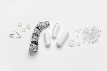 Spools of thread with ball pins, buttons and measuring tape on white background