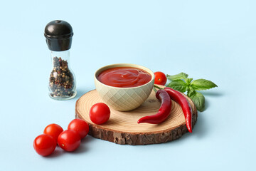 Bowl of tasty tomato sauce with chili peppers and basil leaves on blue background