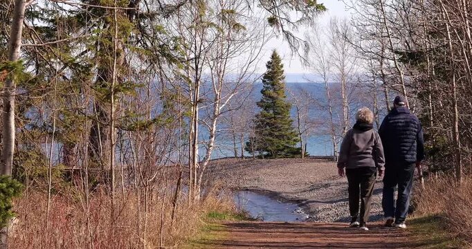 Senior couple walk on a path toward the North Shore of Lake Superior on a sunny spring day in northern Minnesota. Minnesota.