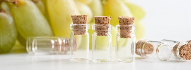 Three clear glass vials with cork stoppers on a white surface, green grapes blurred behind; concept of grape sample testing and food lab research. Photo