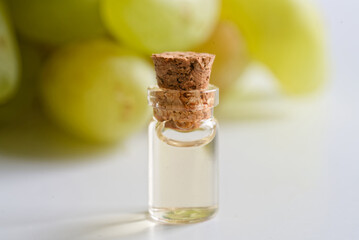 Mini glass vial with grape juice, cork sealed, on white with soft grape cluster bokeh; concept of sampling, food lab research and quality control in winemaking. Photo