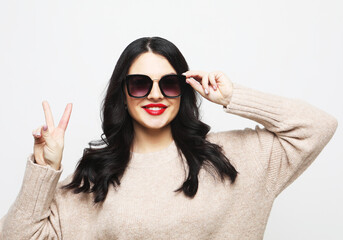 Portrait of young woman wearing sunglasses showing victory sign near face