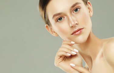 A beautiful young woman with a perfect face touches her facial skin with her fingertips.