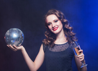 Young happy woman in evening dress holding champagne and disco ball. Brighrt make up and Wavy hairstyle.