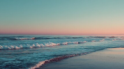 Obraz premium Gentle waves wash ashore on a sandy beach under a pastel sky.