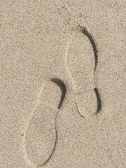 Footsteps and shoe prints on sandy ground. Visible footprints on soil and in the sand, captured from a top-down view. Footprints from shoes and sandals scattered across brown sand of sandpit or  beach