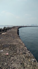 Rocky coastline and sea wall of the harbor. With white clouds and harbor in the background. Stone embankment