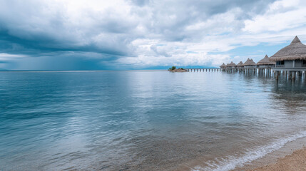 Fototapeta premium Tranquil Turquoise Ocean Scene with Gentle Rolling Waves Under a Cloudy Sky and Overwater Bungalows on the Horizon