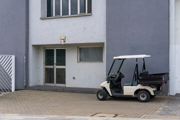 Electric transport cart parked near gray plaster building, small utility vehicle standing on paving stone surface in front © Adam