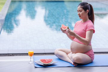 A pregnant woman in a red outfit sits by the pool, holding a slice of watermelon with orange juice beside her. The image conveys health, relaxation, and a calm, refreshing maternity lifestyle.