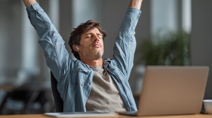 Young man stretching and relaxing at desk with laptop in office  