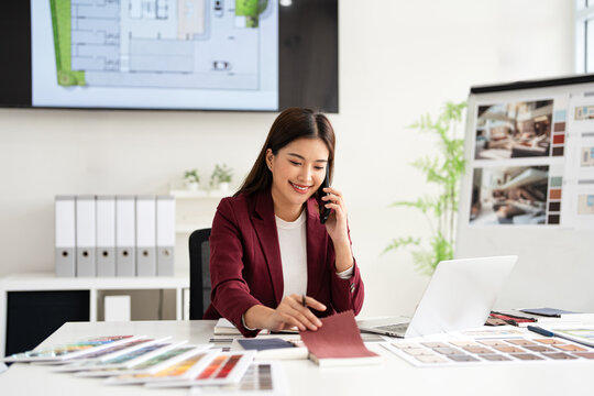 Happy interior designer speaking over the phone in her home office. Creative business woman taking notes during a phone call with her clients. Female designer working on a new project remotely.