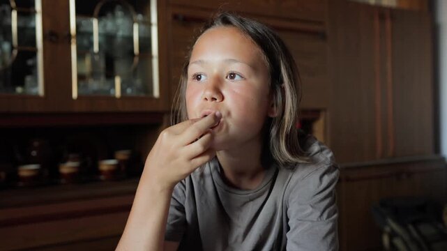 Child tasting small snack at table, pensive expression in warm wooden kitchen, slow thoughtful bites and subtle savoring gestures, closeup portrait with natural light