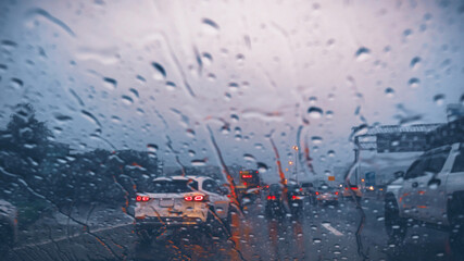 Atmospheric view of heavy rain on the highway at dusk, with raindrops on the windshield and blurred taillights