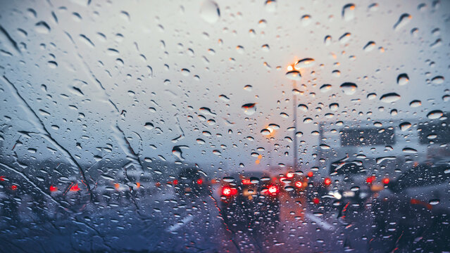 Atmospheric view of heavy rain on the highway at dusk, with raindrops on the windshield and blurred taillights