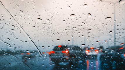Atmospheric view of heavy rain on the highway at dusk, with raindrops on the windshield and blurred taillights