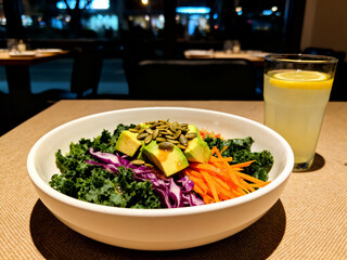 A fresh kale and red cabbage salad topped with avocado slices, shredded carrots, and pumpkin seeds, served with a glass of lemonade at a restaurant table.