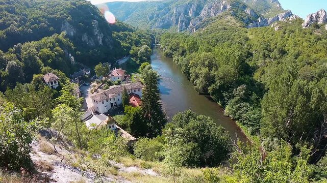 High-altitude aerial video of the Cherepish Monastery in the Iskar Gorge, showing the monastery, the winding river, and surrounding mountain ridges on a bright summer day.