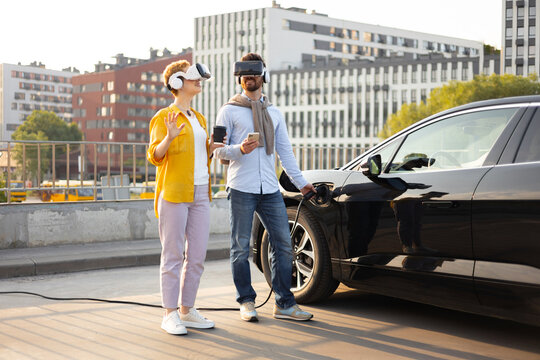 A couple wearing VR headsets while their electric vehicle charges in an urban setting. - Powered by Adobe