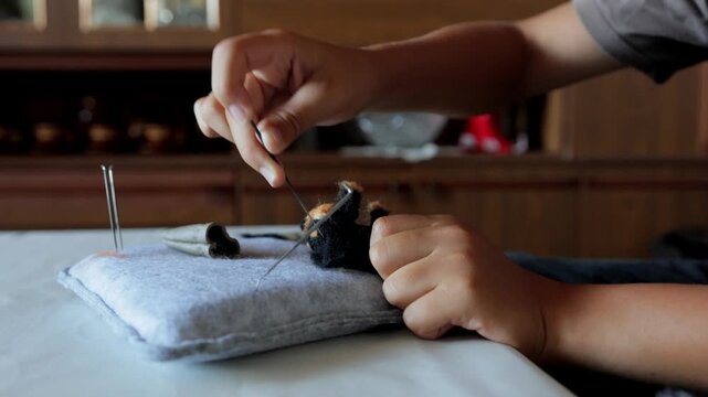 Closeup of hands skillfully crafting with needles and felt, Focused view of hands meticulously creating small animal sculpture using felting tools in cozy studio setting