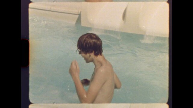 Fourteen year old boy and his eight year old sister sliding side by side into a pool on a sunny day captured on real film
