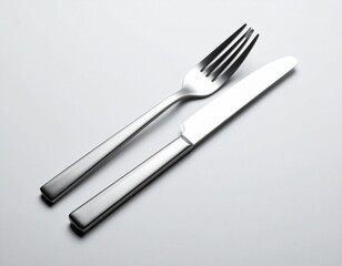 A set of sleek stainless steel cutlery, a fork and a knife, arranged on a clean white table for dining and etiquette
