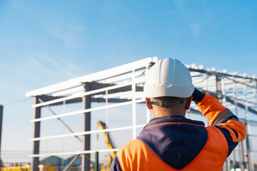 Builder posing in front of steel frame structure under construction