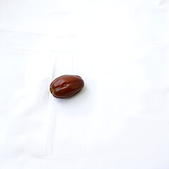 A solitary, plump, and vibrant Date fruit with a smooth brown skin and a subtle sheen, placed gently on a crisp, linen white background