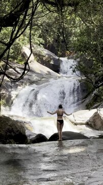 bold girl in bikini walks on rocks near famous natural slide admiring powerful Josephine Falls, Wooroonooran National Park, near Cairns, Queensland, Australia