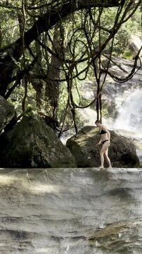 bold girl in bikini walks on rocks near famous natural slide admiring powerful Josephine Falls, Wooroonooran National Park, near Cairns, Queensland, Australia