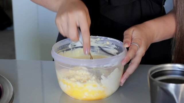 Blending ingredients in bowl, Hands combining dense mixture with focus, Precise hand techniques emphasize mixing substantial batter with yolks visibly embedded in dish