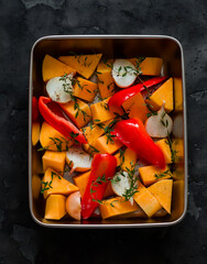Ingredients for making pumpkin soup - pumpkin, sweet pepper, onion, garlic, thyme, olive oil in a baking dish on a dark background