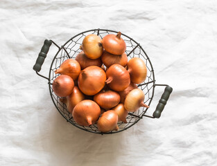 Onions in a metal basket on a light background, top view