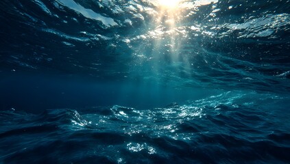 Obraz premium Sunlight streams through the ocean surface illuminating the deep blue water with shimmering light rays creating a serene and tranquil underwater scene