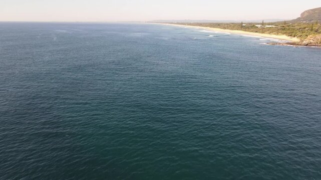 Drone aerial moving forward over a blue ocean during sunrise at Coolum beach