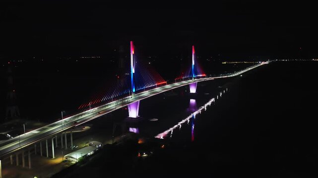 Stunning aerial footage showcases the colorful illumination of the Heroes del Chaco Bridge in Asuncion, Paraguay. Nighttime lighting reflects vibrantly in the water below.