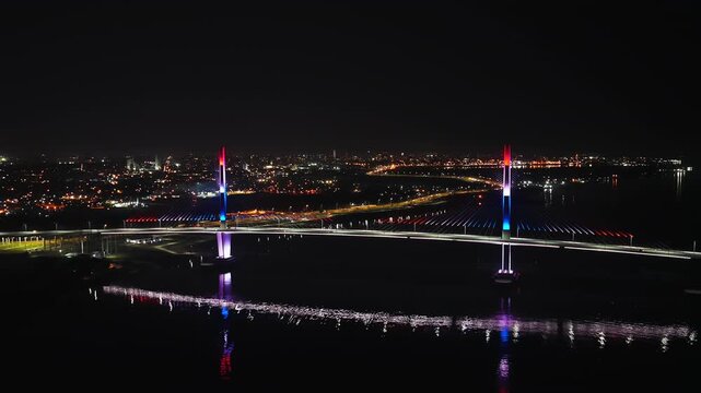 Dramatic aerial footage over Asuncion, Paraguay, showcasing the illuminated Puente Heroes del Chaco at night. The vibrant cityscape glows under the serene night sky.