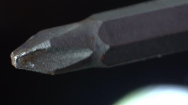 Close-up of a metal Phillips head screwdriver bit on a dark background