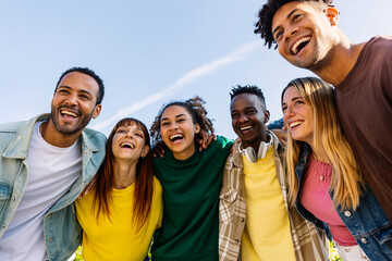 Young group of diverse people having fun together standing together outside. Millennial generation student friends hugging each other while laughing outdoor in a sunny day. Friendship concept
