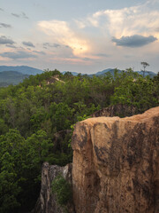 Majestic Pai Canyon at sunset, showcasing dramatic rugged cliffs and lush green forests stretching towards distant mountains under a warm, cloudy sky. A breathtaking natural landscape in Thailand.