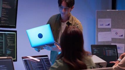 Group of young Asian developers collaborating during nighttime coding session. Team reviewing software issues and debugging source code in dark modern tech workspace. Innovation and teamwork in action - Powered by Adobe