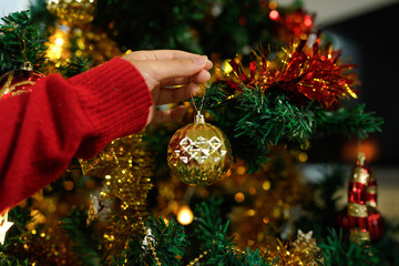 Hands decorating Christmas tree with ornaments and lights for festive holiday celebration