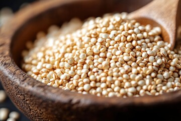 Close-up of a wooden spoon filled with small round beige quinoa grains in a wooden bowl, showcasing natural texture and earthy tones