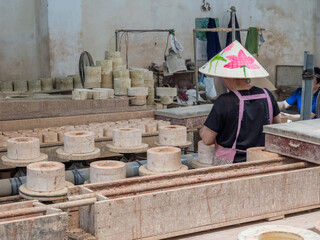 A worker wearing a traditional Vietnamese conical hat with a lotus flower design meticulously...