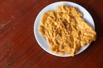 Fried omelet in white plate placed on wooden table
