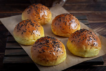 Homemade freshly baked plain golden brown soft hamburger buns topped with sesame seeds against wooden background. Homebaking, freshness, bbq concept