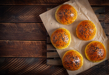 Homemade freshly baked plain golden brown soft hamburger buns topped with sesame seeds against wooden background. Homebaking