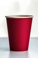 Close-up of a plain red disposable paper cup standing on a light surface with a soft blurred white and gray background