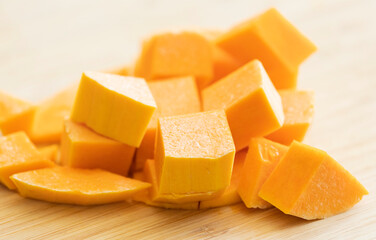chopped cubes of butternut squash and pumpkin on wooden cutting board close up